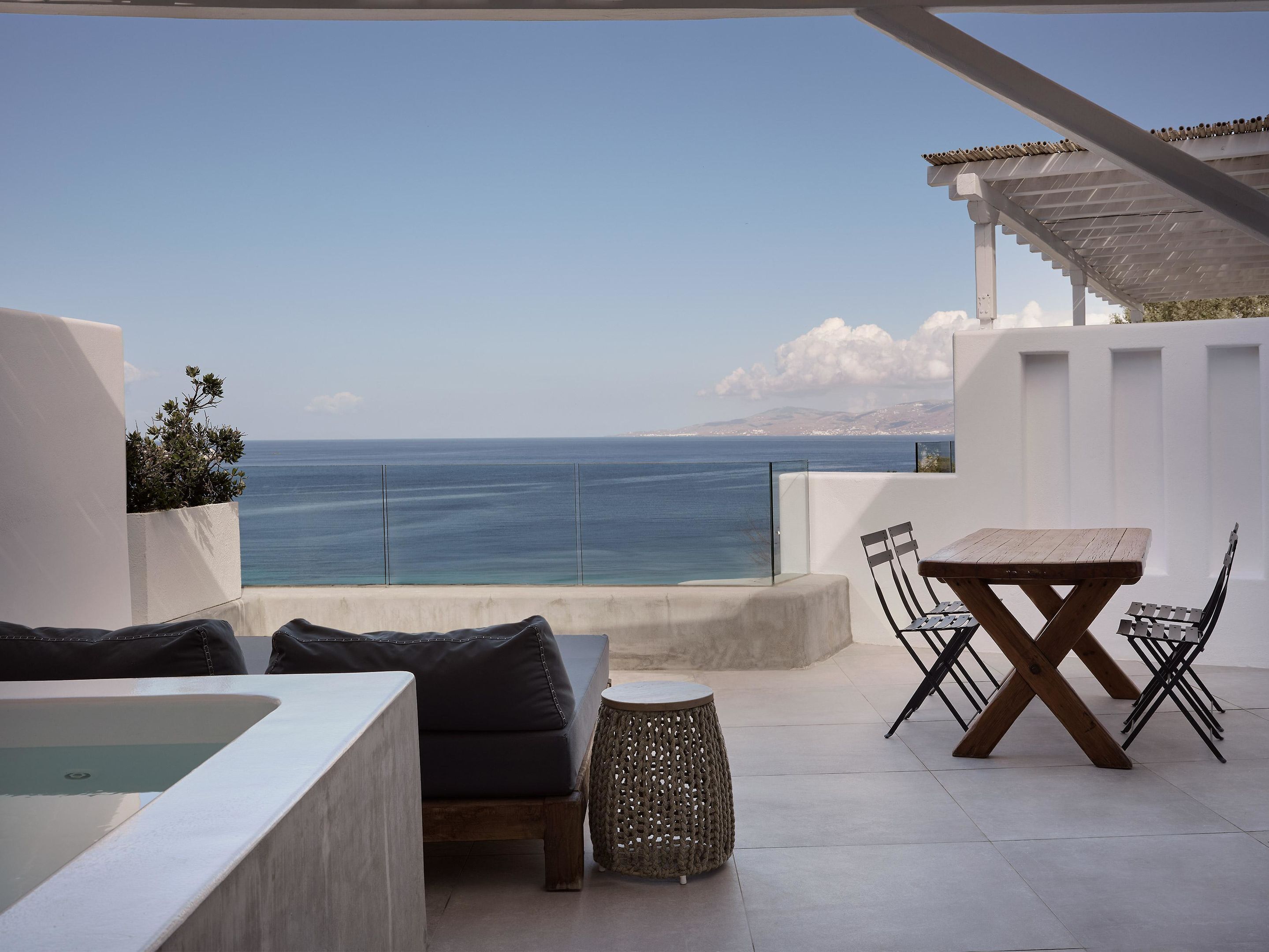 Un área de estar al aire libre con vista al mar, una mesa, sillas y una pequeña mesa redonda.