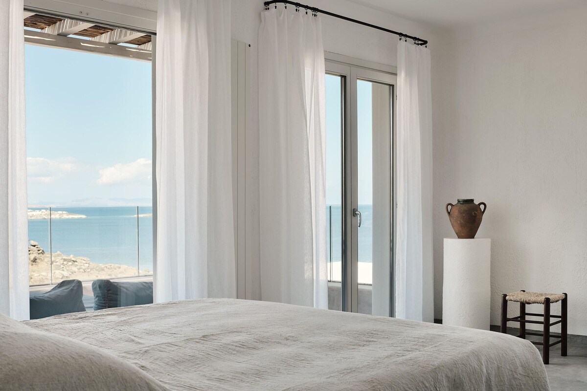 Ein Schlafzimmer mit einem großen Bett, Meerblick und einer rustikalen Vase auf einem Sockel.