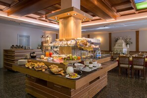 Un buffet de petit-déjeuner proposant une grande variété d’aliments, notamment des viennoiseries, des fruits et des boissons, installé dans une pièce bien éclairée, dotée de meubles en bois et agrémentée d’un élément décoratif central.