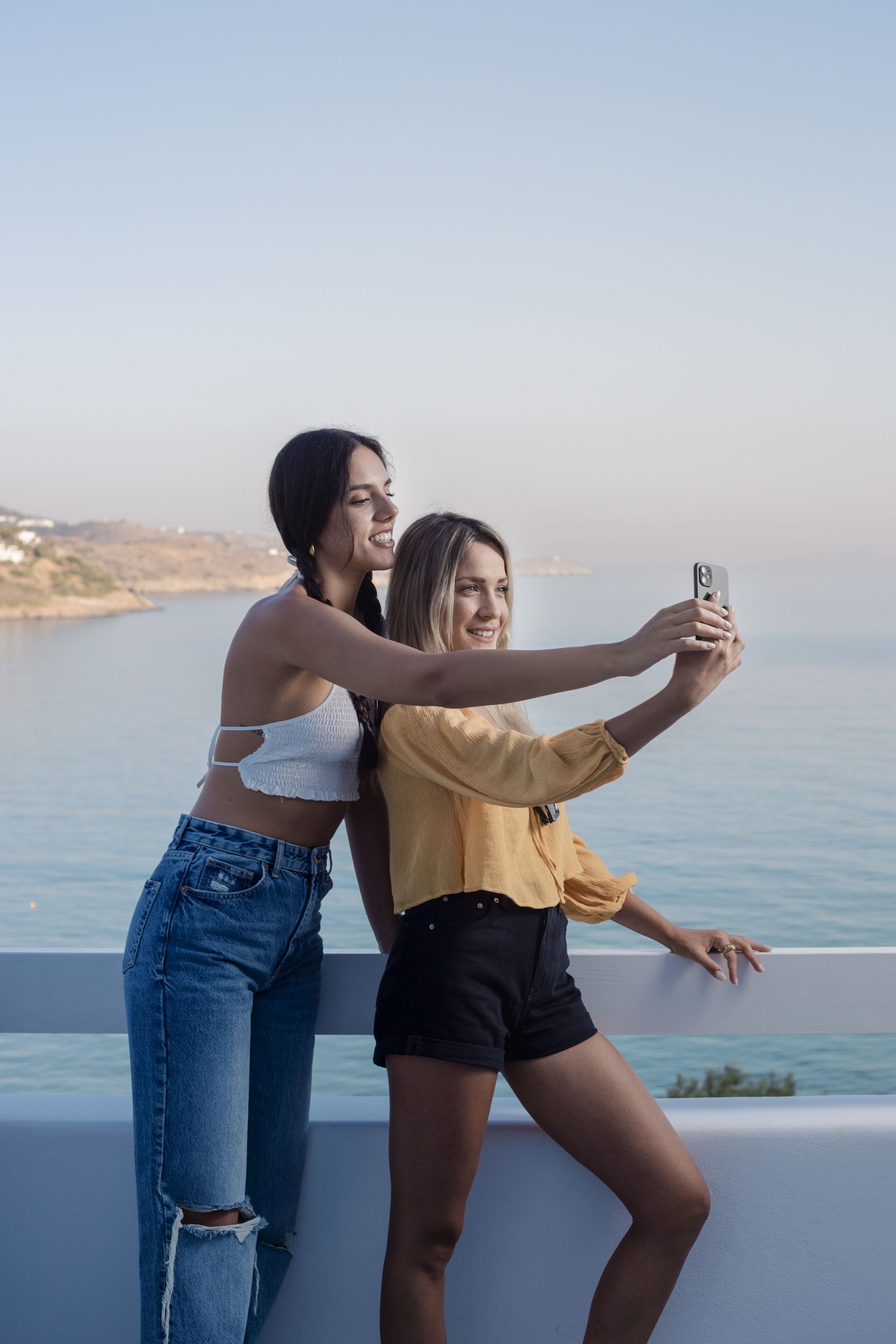 Two people taking a selfie by a balcony overlooking a body of water.