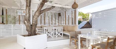 An outdoor patio area with white furniture, a tree planter, and a hanging basket.