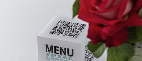 Valkoinen laatikko, jonka päällä on QR-koodi ja teksti ”MENU”, on sijoitettu valkoiselle alustalle, ja sen vieressä on ruusukimppu.