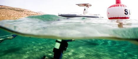 An underwater view of a person snorkeling with fins, a boat with a flag, and a buoy with a flag.