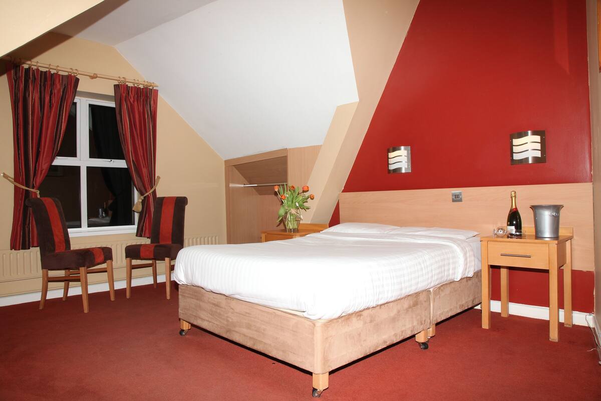Ein Schlafzimmer mit Bett, zwei Stühlen, einem Nachttisch und einer roten Akzentwand.