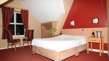 A bedroom with a bed, two chairs, a nightstand, and a red accent wall.