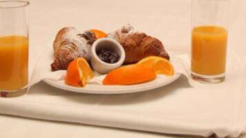 Ein Frühstücksteller mit Croissants, Orangenscheiben und einer kleinen Schale Marmelade, dazu zwei Gläser Orangensaft.