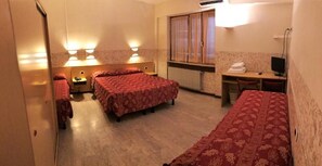 Una camera d'albergo con due letti, una scrivania, una sedia e una finestra con tende.