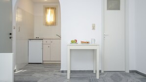 A modern kitchen with white cabinets, a small refrigerator, and a table with fruits and a pitcher. - Soula Naxos (Naxos)