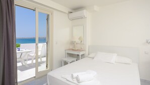A hotel room with a bed, a desk, a chair, a lamp, and a view of the sea. - Soula Naxos (Naxos)