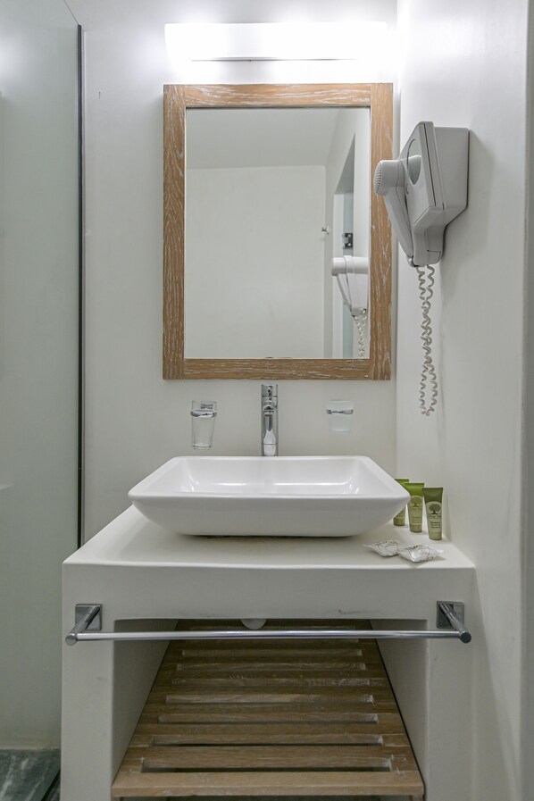A bathroom with a white sink, a wooden-framed mirror, a hairdryer, and a towel rack. - Soula Naxos (Naxos)