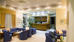 A hotel lobby with a reception desk, seating area with sofas and chairs, a potted plant, and a staircase leading to the upper floors. - Astali Hotel (Rethymno)