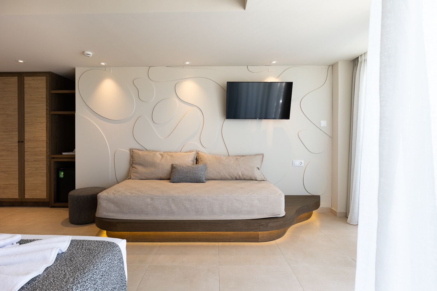 Un dormitorio moderno con cama, televisor montado en la pared y armario de madera.