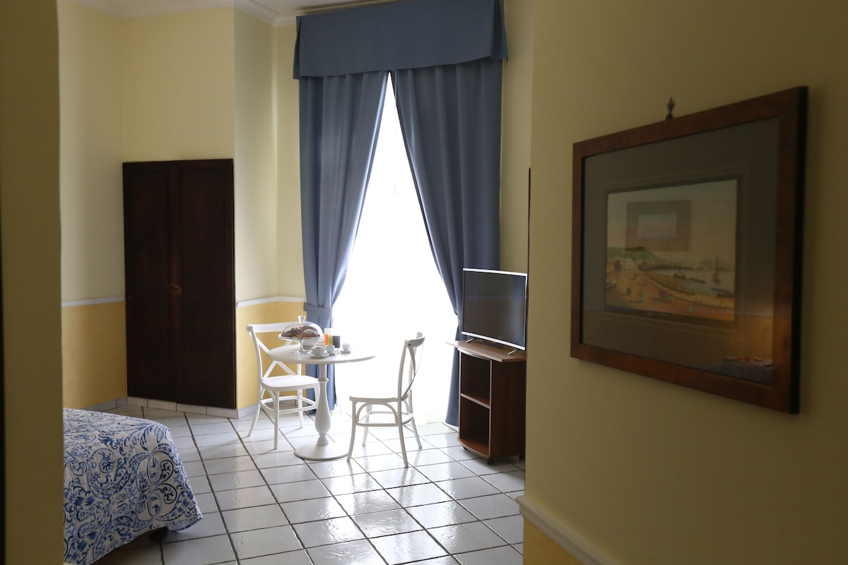 A room with a bed, a desk, a chair, a TV, and a painting on the wall.