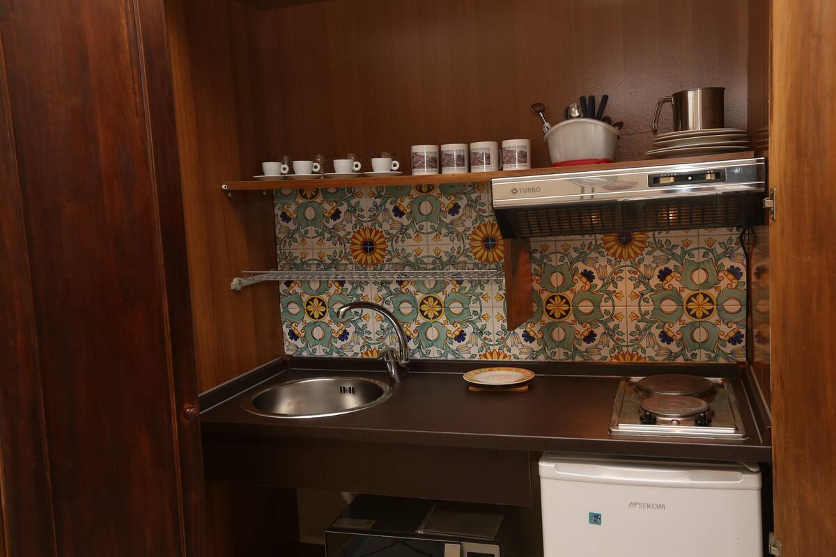 Una cocina compacta con pileta, estufa y un estante con tazas y una olla.