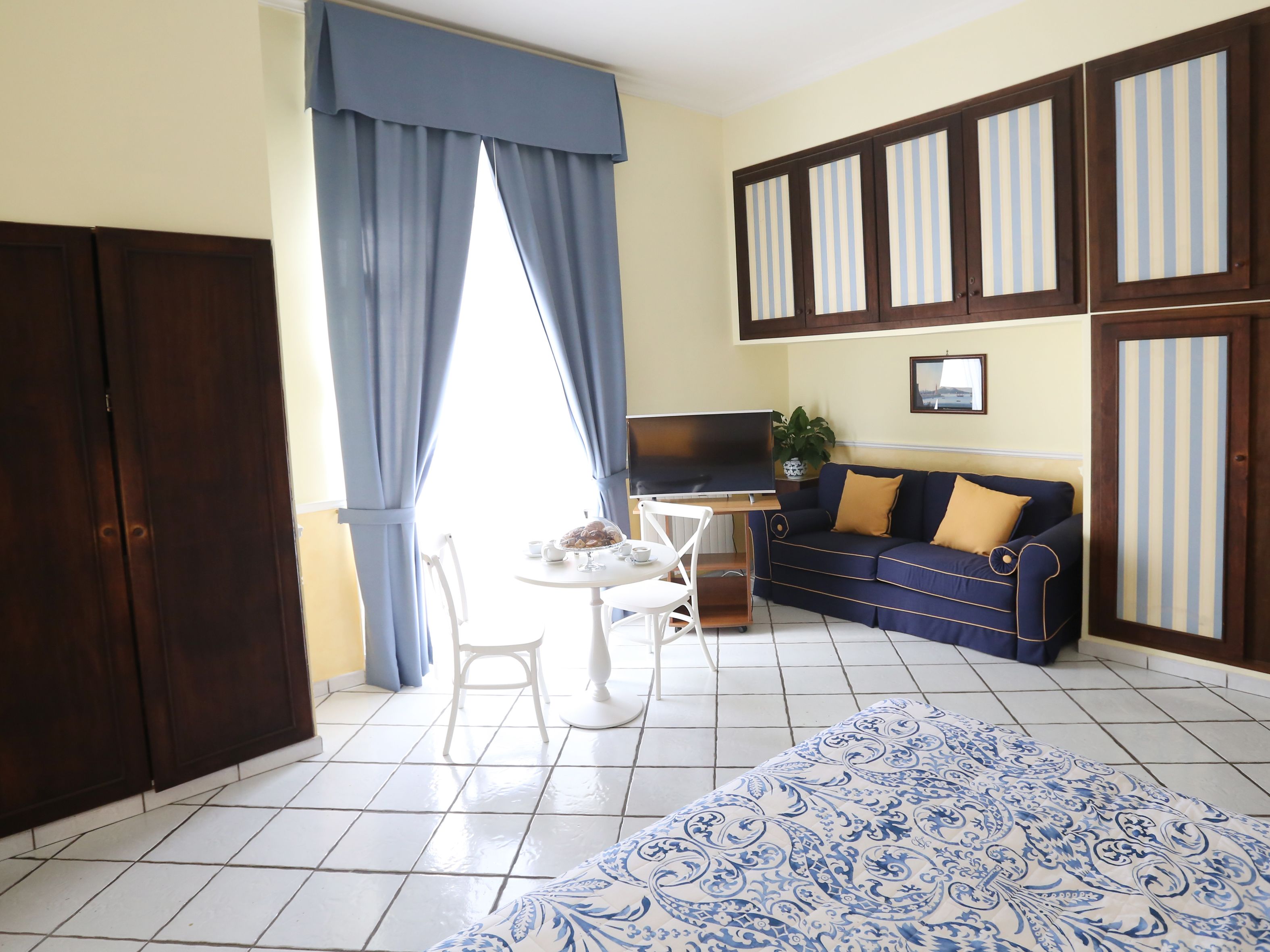 A room with a bed, a desk with a computer, a sofa, a chair, and a TV.
