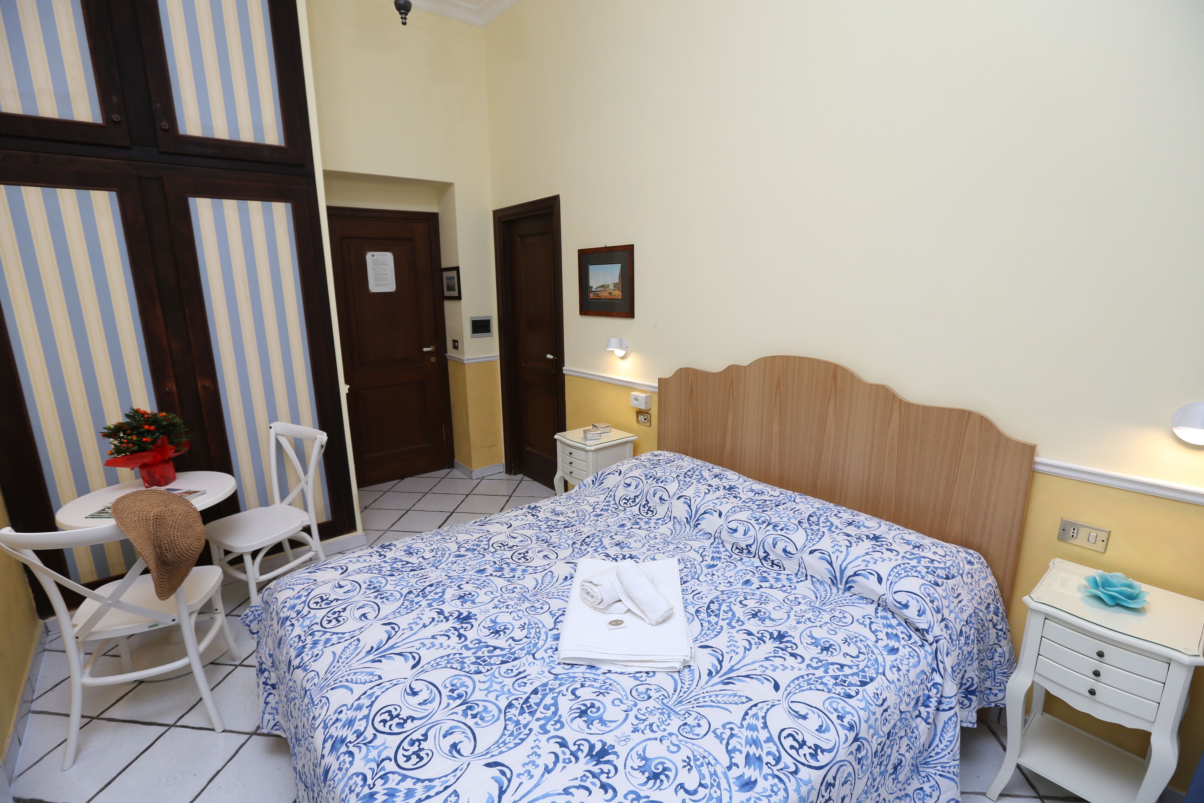A bedroom with a bed, a chair, a small table with a lamp, and a picture on the wall.