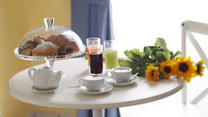 A white table with a teapot, two cups, a glass of juice, a glass of red juice, a glass of green juice, a plate with pastries, and a bouquet of sunflowers. - B&B Santa Lucia 50 (Naples)