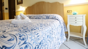 A neatly made bed with a blue and white patterned bedspread and rolled white towels. There is a white bedside table with a blue decorative item on top. - B&B Santa Lucia 50 (Naples)