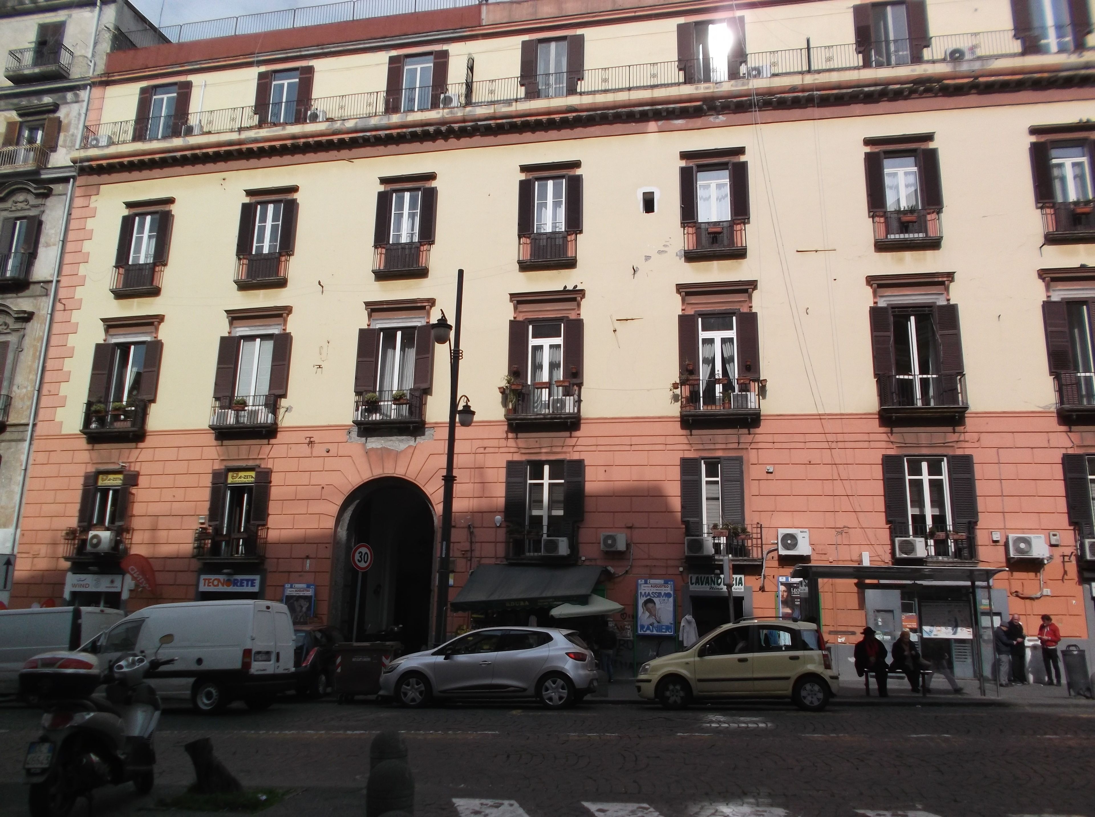 A multi-story building with a red brick facade, multiple windows with shutters, and a central entrance.