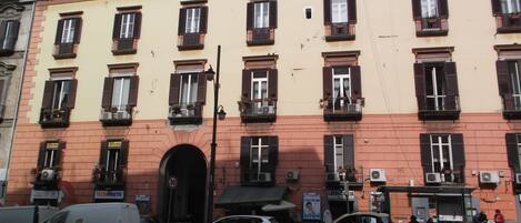 A multi-story building with a red brick facade, multiple windows with shutters, and a central entrance.