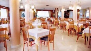 Un comedor amplio con varias mesas y sillas, pilares grandes y lámparas colgantes.
