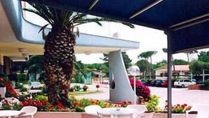 Un espacio al aire libre con sillas y mesas de plástico blanco, rodeado de diversas plantas y flores.