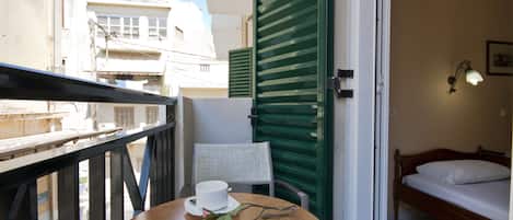 A balcony with a table, a chair, a rose, and a bed with a white pillow.