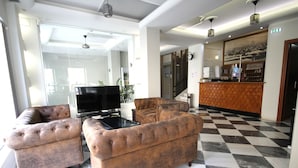 A lobby with two tufted sofas, a flat-screen TV, a checkered floor, and a reception desk with a cityscape mural. - Mirabello Hotel (Heraklion)