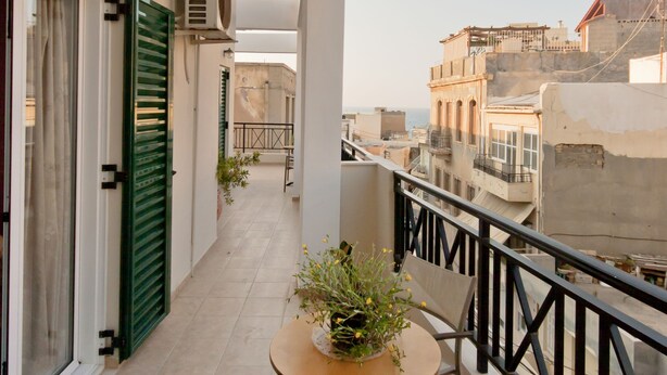 A balcony with a table and chairs, a potted plant, and a view of buildings. - Mirabello Hotel (Heraklion)