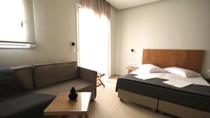 A modern hotel room with a sofa, a small table, a bed with pillows, and a nightstand. - Mirabello Hotel (Heraklion)