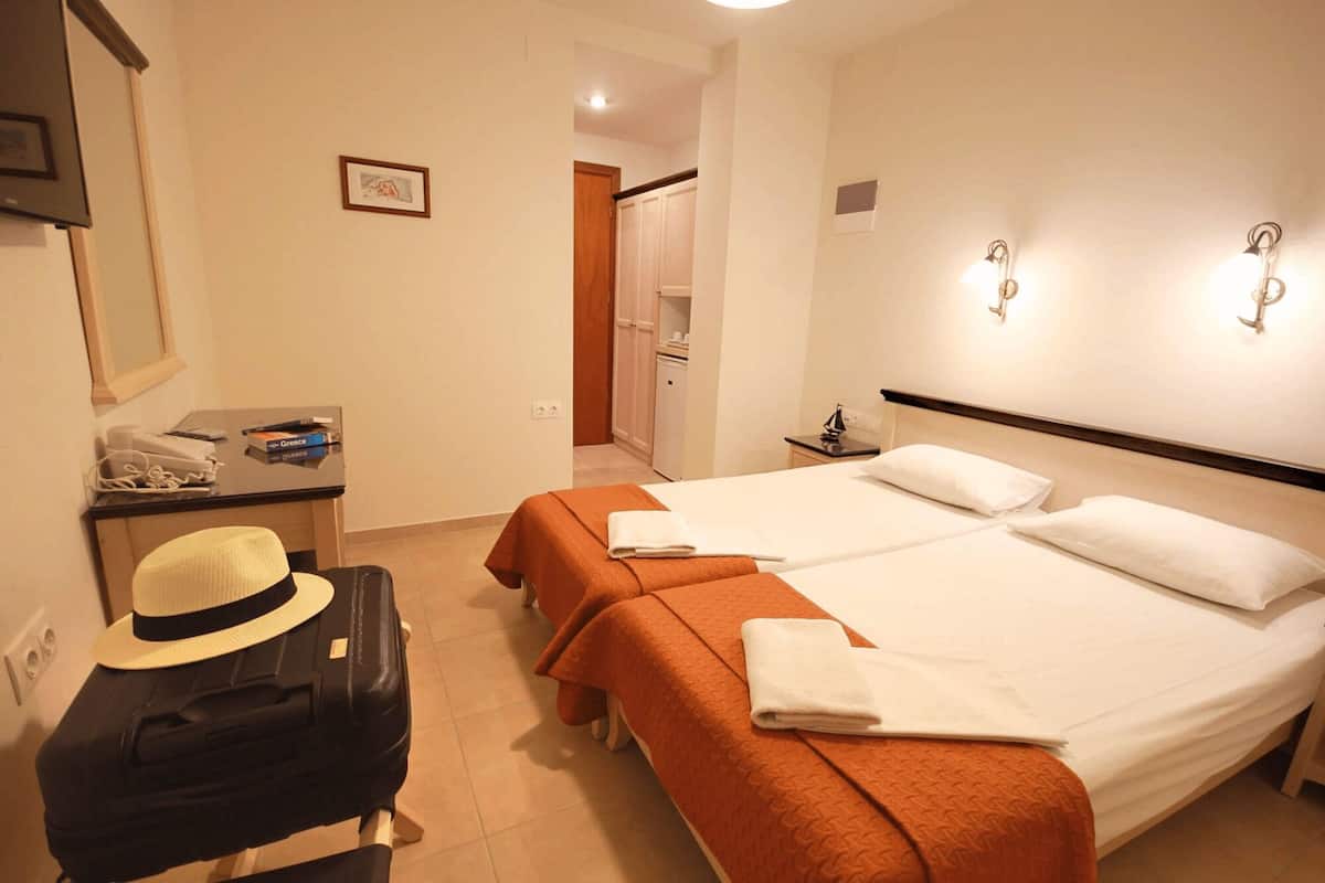 Une chambre d’hôtel avec deux lits, un bureau avec un ordinateur, une valise et un chapeau posé sur le sol.
