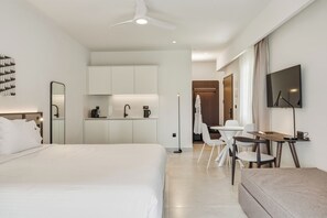 Una habitación de hotel moderna con una cama grande, un escritorio, una silla, una pequeña cocina y un televisor.