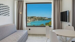 A modern room with a large window, a grey sofa, a round table with chairs, and a flat-screen TV mounted on the wall. - Scala Boutique Hotel & Suites – Adults Only (Malevizi)