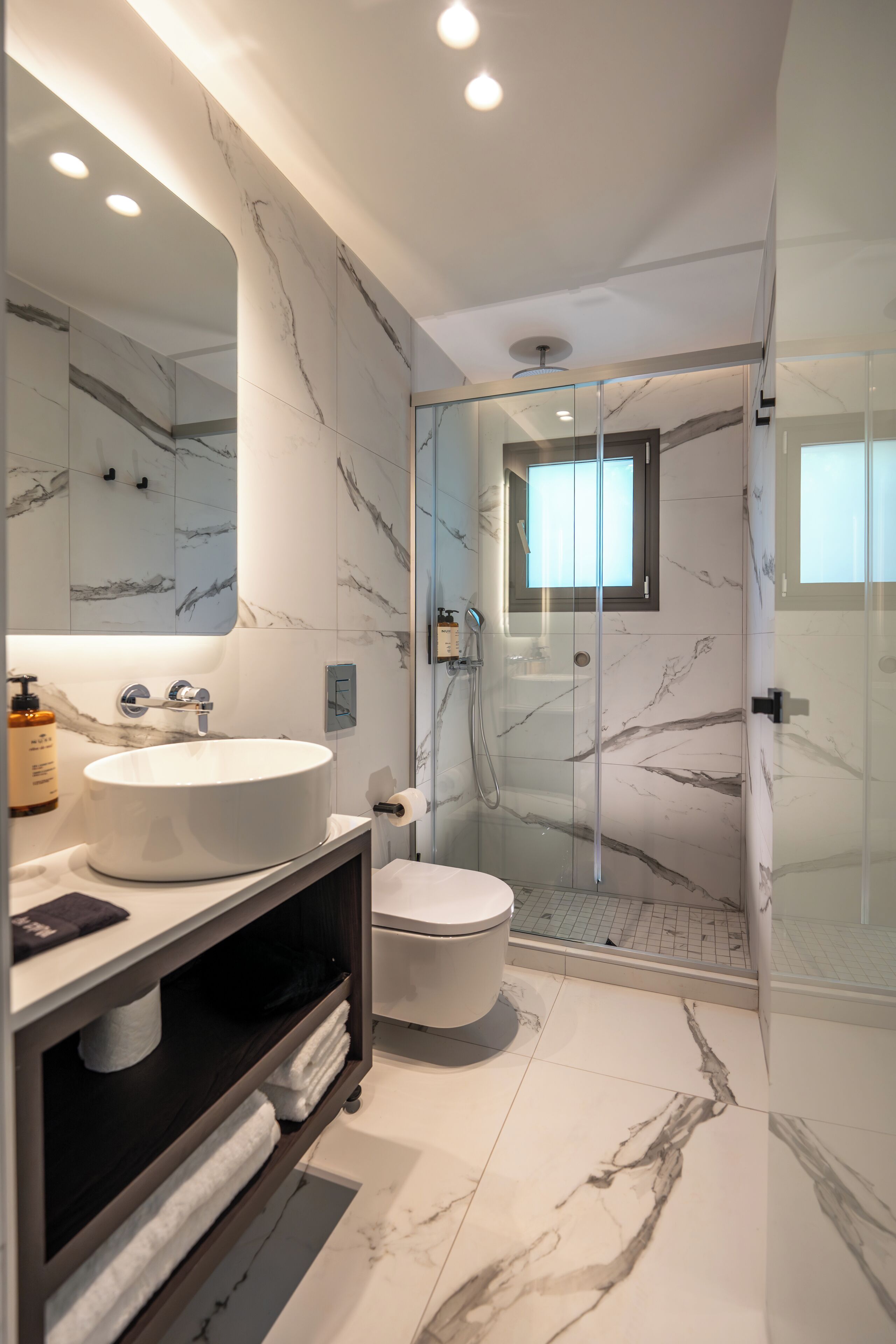 Un bany modern amb un mirall gran, un lavabo rodó, un vàter i una dutxa amb envàs de vidre.