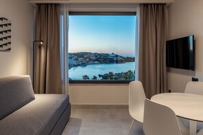 A modern hotel room with a large window offering a city view, a flat-screen TV, a sofa, and a dining table. - Scala Boutique Hotel & Suites – Adults Only (Malevizi)