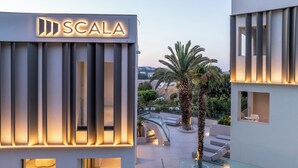 A modern building with a 'SCALA' sign, featuring a glass balcony with outdoor seating and a palm tree. - Scala Boutique Hotel & Suites – Adults Only (Malevizi)