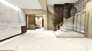 A modern lobby with marble flooring, a glass staircase, and a decorative wall panel. - Kronio (Archaia Olympia)