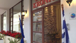 The exterior of Hotel Kronio with a stone facade, large windows, and two flags. - Kronio (Archaia Olympia)