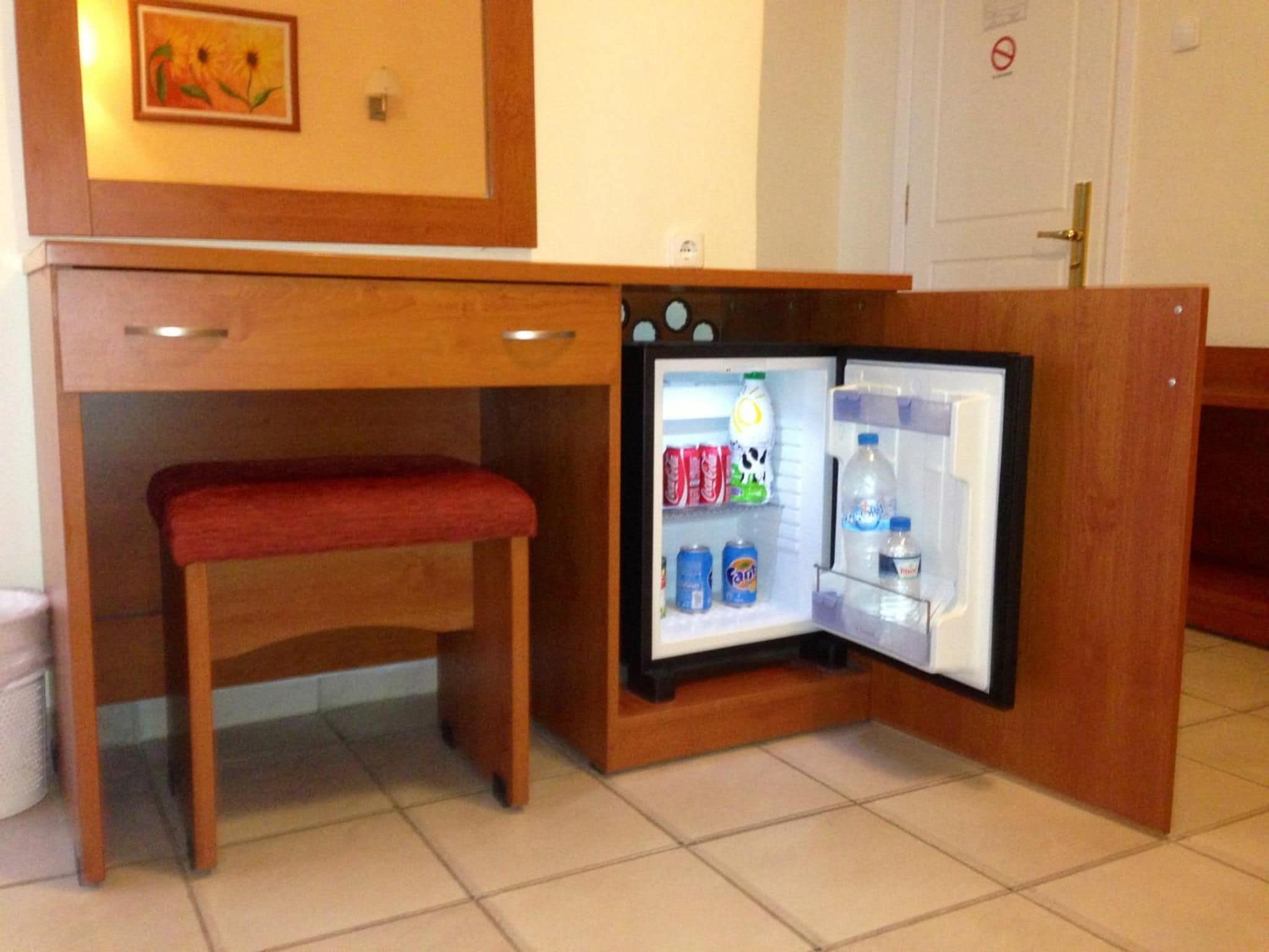 A compact refrigerator with a bench underneath, containing beverages and a bottle of water.