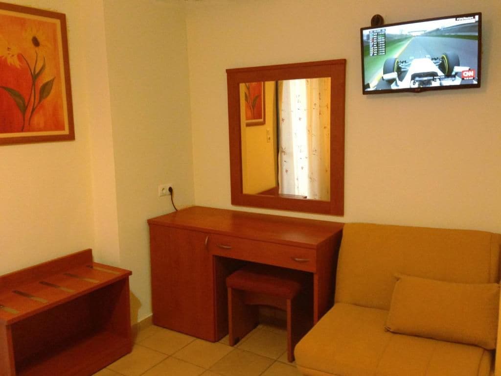 Una habitación con un escritorio de madera, un espejo, un televisor y un sofá.
