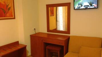 Una habitación con un escritorio de madera, un espejo, un televisor y un sofá.