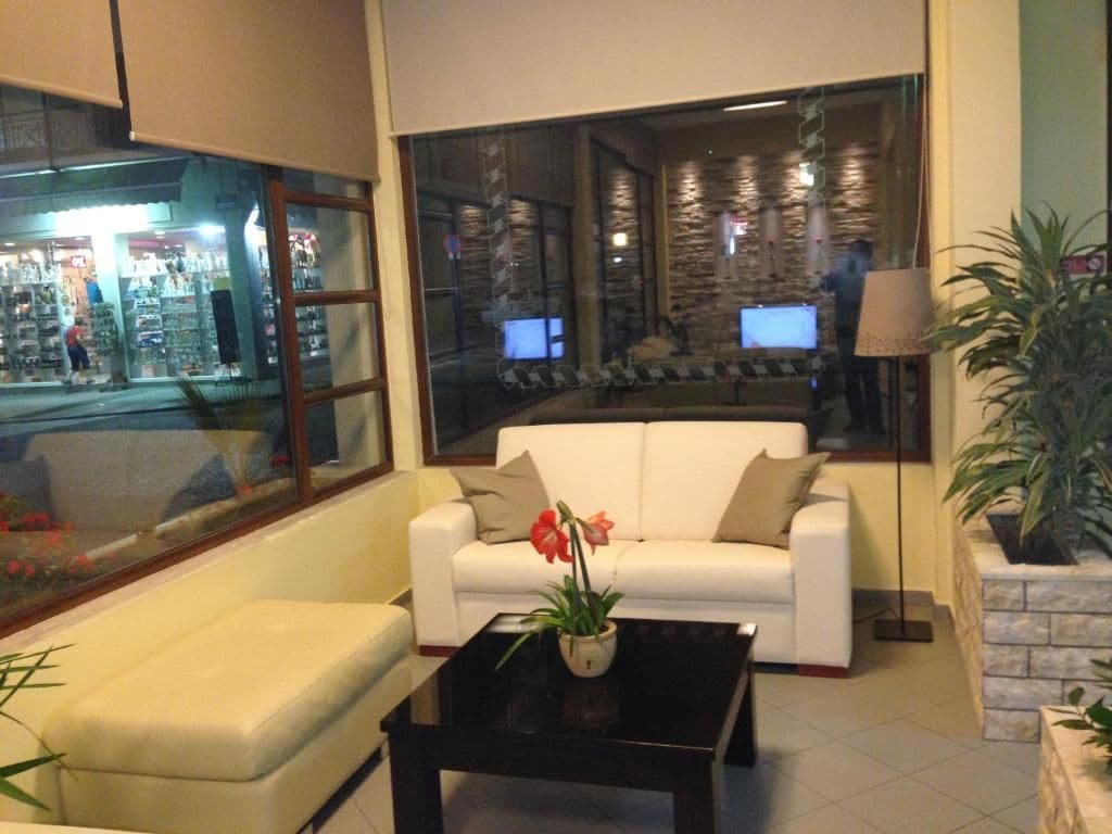 Una sala de estar con un sofá blanco, una mesa de centro negra con una planta y un ventanal con vistas a una tienda y un edificio con múltiples pantallas.