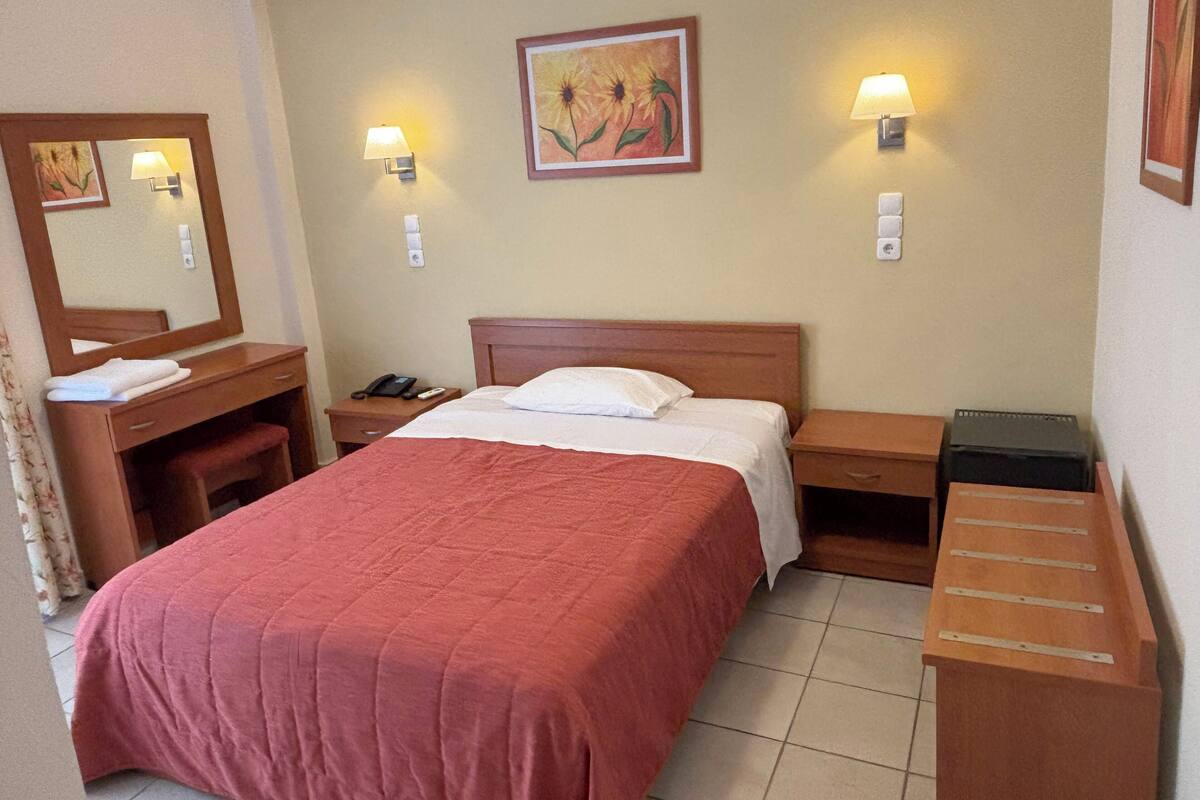 A hotel room with a bed, a desk, a chair, a telephone, and a painting on the wall.