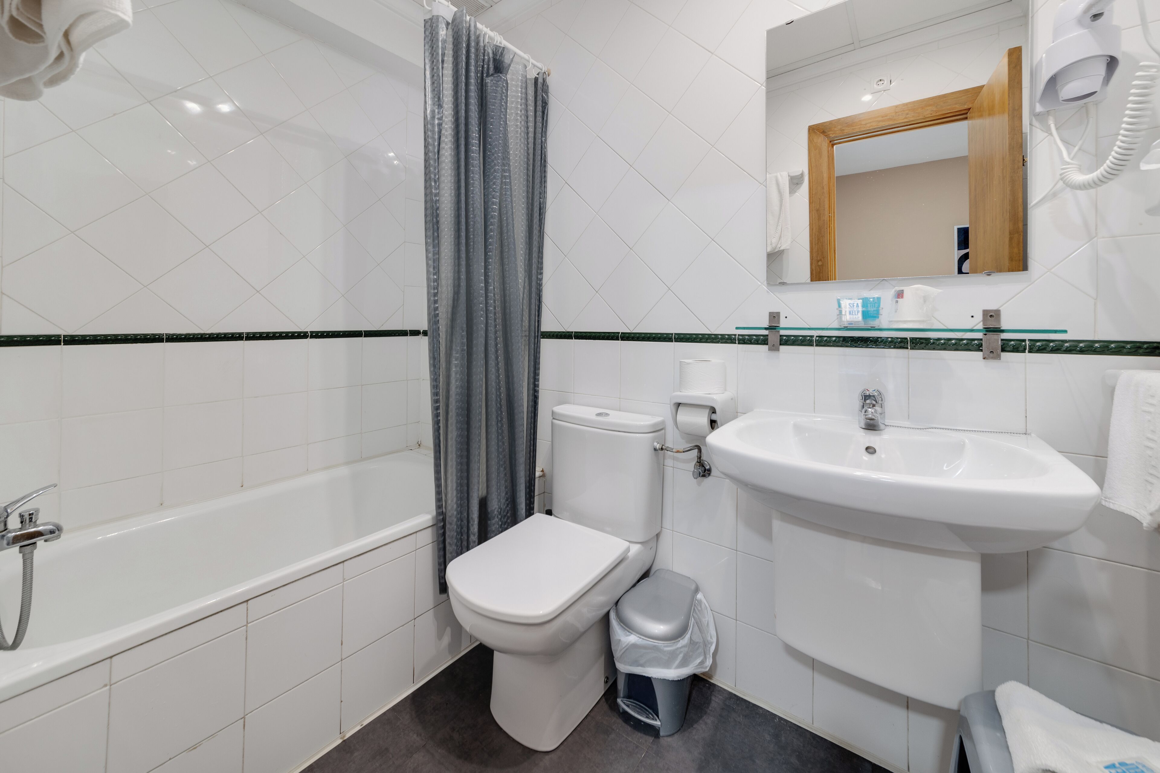 A bathroom with a bathtub, toilet, sink, and a mirror with a hairdryer.