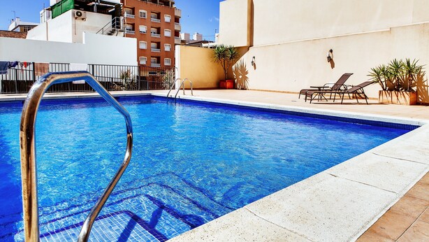 A swimming pool with a metal ladder, lounge chairs, and potted plants. - Hotel Madrid (Torrevieja)