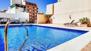 Una piscina al aire libre, sombrillas, sillones reclinables de piscina