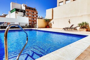 A swimming pool with a metal ladder, lounge chairs, and potted plants. - Hotel Madrid (Torrevieja)