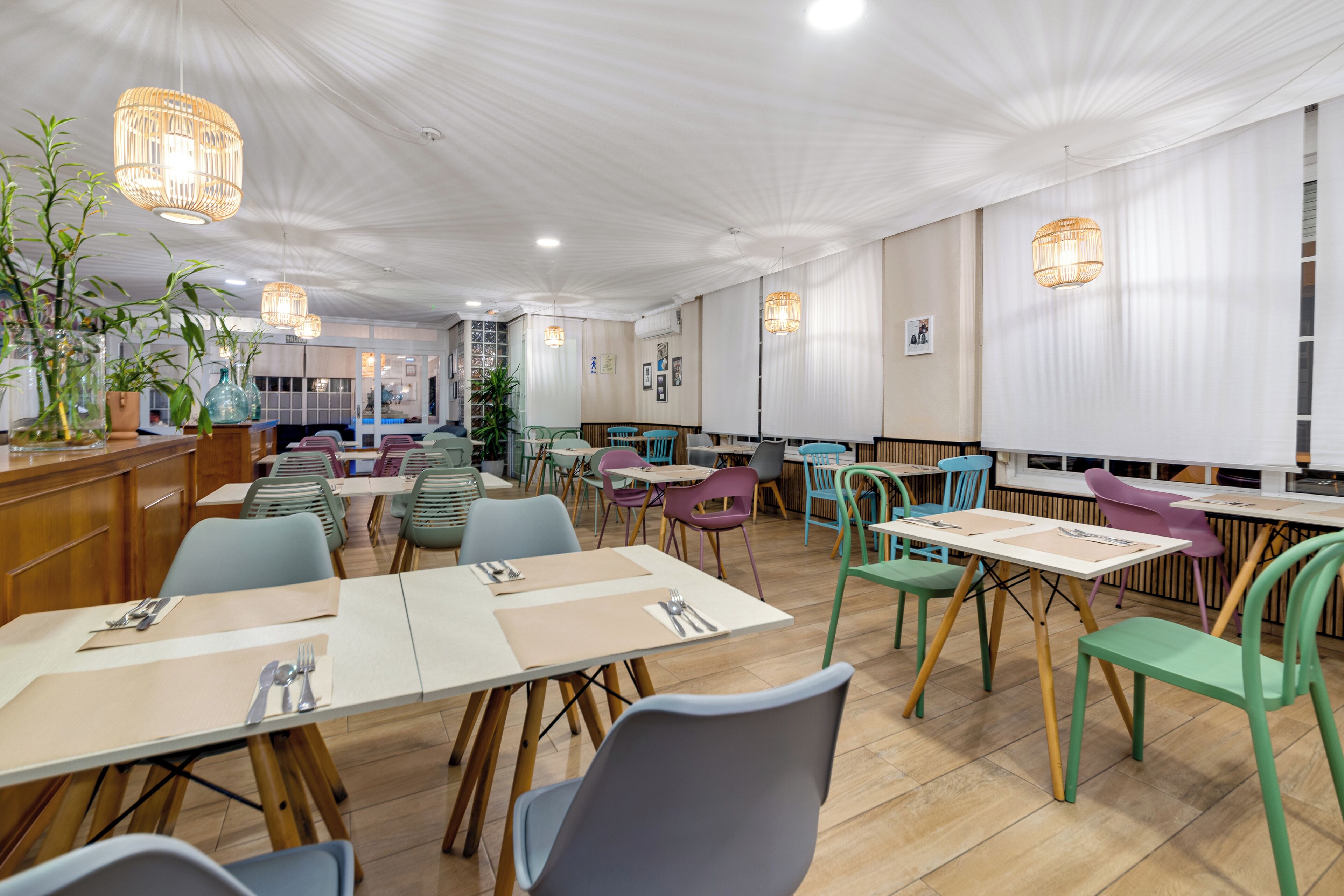 A restaurant with multiple tables and chairs, a wooden counter, and hanging lights.