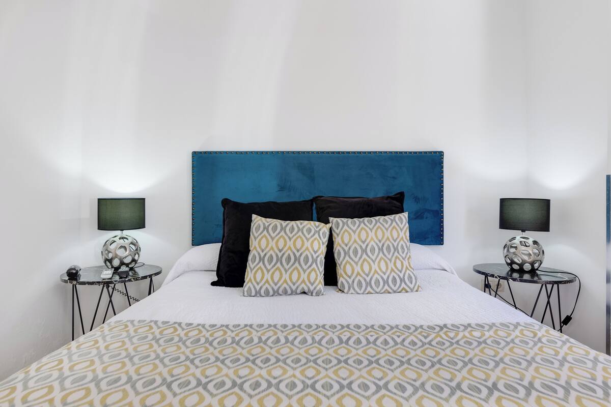 A neatly made bed with patterned bedding, two bedside tables with lamps, and a blue headboard.