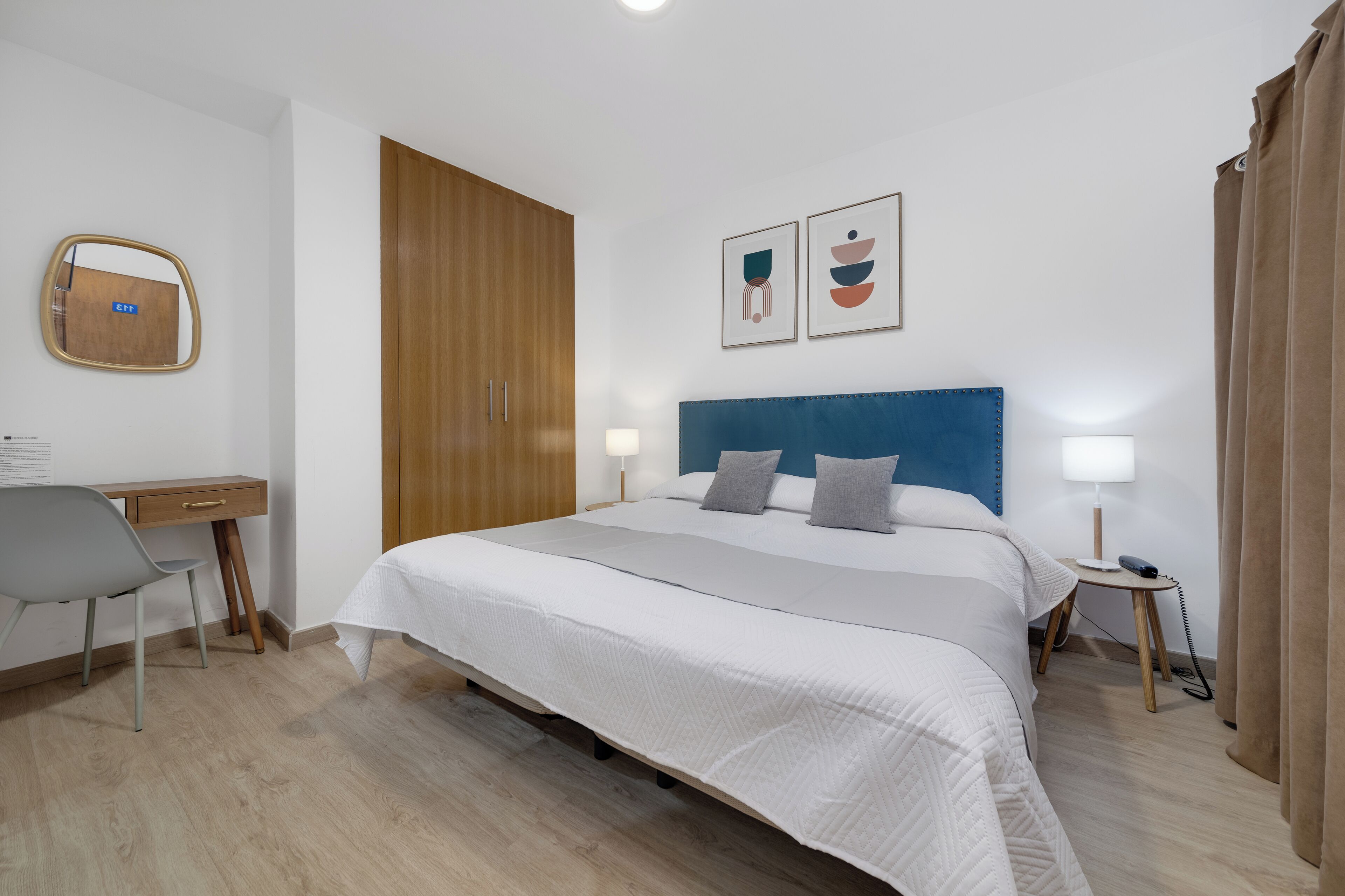 Habitación de hotel ordenada con una cama grande, un escritorio y una silla. Hay dos mesitas de noche con lámparas.